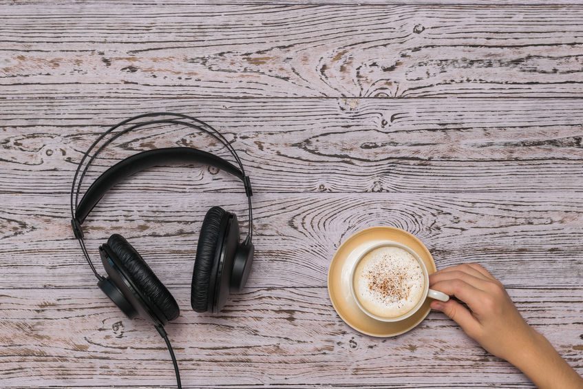 Hand holding a coffee Cup and black wired headphones on the wooden table. Coffee break during work.